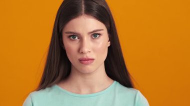 Kızgın genç bir kadın kameraya bakıyor. Stüdyonun turuncu arka planında izole bir şekilde duruyor.