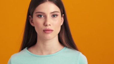 Kafası karışmış genç bir kadın omuzlarını silkiyor. Stüdyoda turuncu bir arka planda tek başına duruyor.