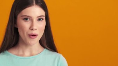 Gülümseyen genç bir kadın, stüdyonun turuncu arka planında tek başına duran yan tarafı işaret ediyor.