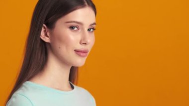 Başarılı genç bir kadın kameraya bakıyor. Stüdyoda turuncu bir arka plan üzerinde izole bir şekilde duruyor.