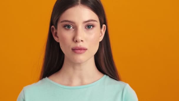 一位积极向上的年轻女子一边点头一边听着观众们孤零零地站在摄影棚里橙色的背景上 — 图库视频影像