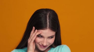 Utangaç genç bir kadının yakın çekim görüntüsü stüdyodaki turuncu bir arka planda izole bir şekilde kameraya bakıyor.