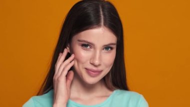 Güzel bir genç kadının yakın çekim görüntüsü stüdyoda turuncu bir arka planda tek başına kameraya poz veriyor.