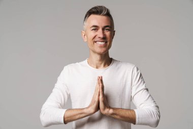 Gri arka planda tek başına dururken meditasyon yapan rahat genç bir adamın portresi.