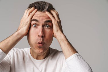 Gri arka planda tek başına dikilen şaşkın, sıradan giyinmiş bir adam.