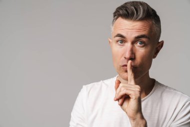 Ciddi bir adam, parmakları dudaklarında Gri arkaplanda bir sır saklıyor