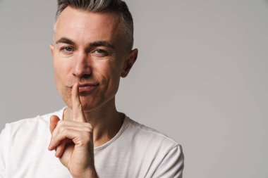 Ciddi bir adam, parmakları dudaklarında Gri arkaplanda bir sır saklıyor