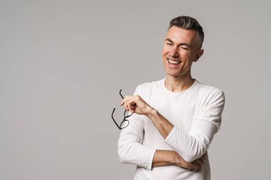 Gri arka planda tek başına durup gülen mutlu bir adam.