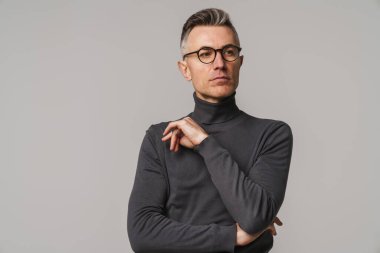 Yakışıklı, kendine güvenen, zeki görünümlü bir adam. Gri arka planda yalnız poz veriyor.