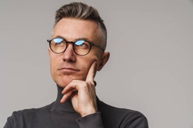 Yakışıklı, kendine güvenen, zeki görünümlü bir adam. Gri arka planda yalnız poz veriyor.