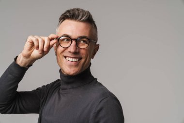 Yakışıklı, kendine güvenen, zeki görünümlü, gri arka planda yalnız poz veren adam.