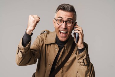 Gri arka planda izole edilmiş, cep telefonu kullanan şık giyinen yakışıklı adam.