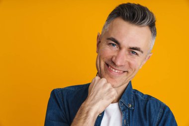 Neşeli yakışıklı adam gülümsüyor ve sarı arka planda izole edilmiş kameraya bakıyor.