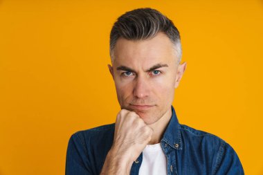 Memnun olmayan yakışıklı adam poz veriyor ve sarı arka planda izole edilmiş kameraya bakıyor.