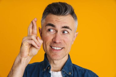 Şans dilemek için dua eden neşeli yakışıklı adam sarı arka planda izole edilmiş.