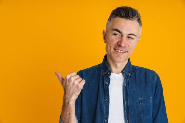 Mutlu yakışıklı adam gülümsüyor ve sarı arka planda izole edilmiş bir şekilde işaret ediyor.