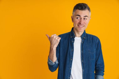 Mutlu yakışıklı adam gülümsüyor ve sarı arka planda izole edilmiş bir şekilde işaret ediyor.