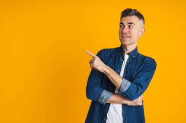 Mutlu yakışıklı adam gülümsüyor ve sarı arka planda izole edilmiş bir şekilde işaret ediyor.