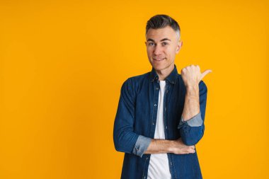 Mutlu yakışıklı adam gülümsüyor ve sarı arka planda izole edilmiş bir şekilde işaret ediyor.