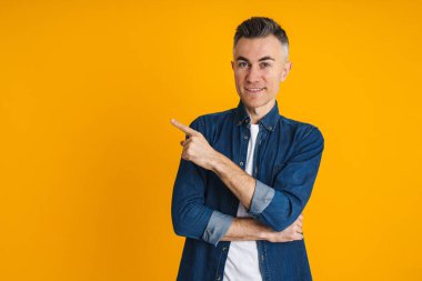 Mutlu yakışıklı adam gülümsüyor ve sarı arka planda izole edilmiş bir şekilde işaret ediyor.