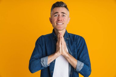 Sarı arka planda avuçlarıyla poz veren mutsuz yakışıklı adam.