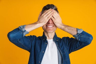 Sarı arka planda gözlerini kapatırken gülümseyen mutlu yakışıklı adam.