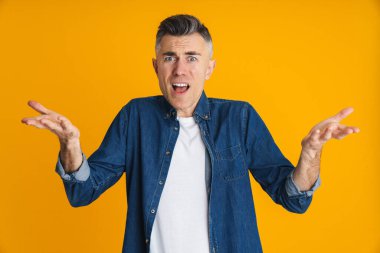 Sarı arka planda elleri açık poz veren hoşnutsuz yakışıklı bir adam.