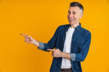 Mutlu yakışıklı adam gülümsüyor ve sarı arka planda izole edilmiş parmakları işaret ediyor.