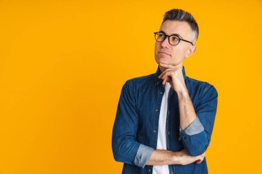Ciddi yakışıklı bir adam sarı arka planda yalnız poz veriyor ve bakıyor.