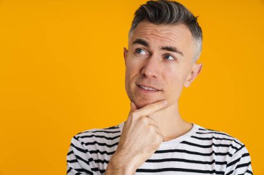 Yakışıklı bir adamın sarı arka planda izole edilmiş bir şekilde poz verdiğini düşünüyor.