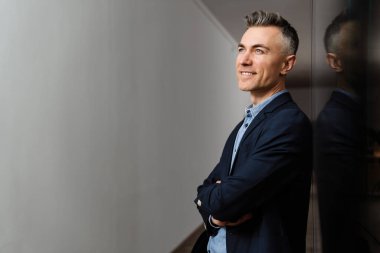 Ofiste duvara yaslanırken gülümseyen ve yukarı bakan mutlu gri adam.