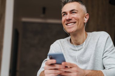 Evde çalışırken cep telefonu kullanan kulaklıklı neşeli bir adam.