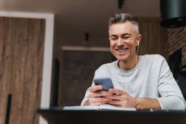 Evde kulaklıkla müzik dinleyen gülümseyen bir adama yaklaş.