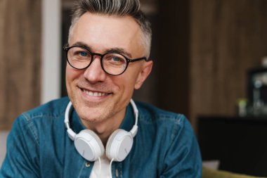 Kulaklıklı, gülümseyen ve kameraya bakan neşeli yetişkin bir adam.