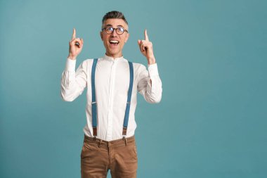 Heyecanlı gözlüklü, gri saçlı adam mavi arka planda, parmaklarını yukarı kaldırarak izole edilmiş.