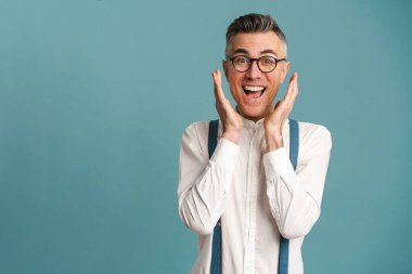 Gözlüklü heyecanlı gri saçlı adam mavi arka planda izole edilmiş kameraya şaşkınlığını ifade ediyor.
