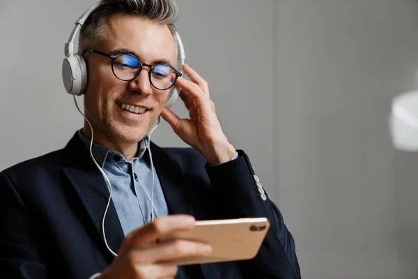 Cheerful grey man in headphones using cellphone while having break at office