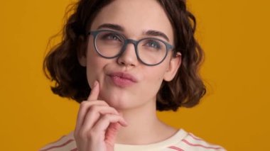 Mutlu genç bir kızın yakın plan görüntüsü stüdyodaki sarı arka planda izole edilmiş bir şeyin hayalini kuruyor.