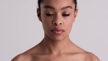 Çekici, yarı çıplak bir kadın kameraya poz veriyor. Stüdyonun gri arka planında tek başına duruyor.