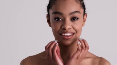 Şaşırmış genç yarı çıplak bir kadın kameraya bakıyor. Stüdyonun gri arka planında tek başına duruyor.