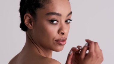 Güzel, genç, yarı çıplak bir kadın kameraya bakıyor. Stüdyonun gri arka planında tek başına duruyor.