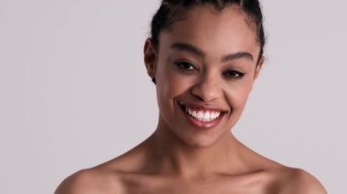 Mutlu, genç, yarı çıplak bir kadın kameraya bakıyor. Stüdyonun gri arka planında tek başına duruyor.