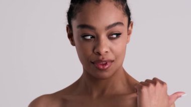 Güzel, genç, yarı çıplak bir kadın, stüdyonun gri arka planında tek başına duran bir tarafı işaret ediyor.