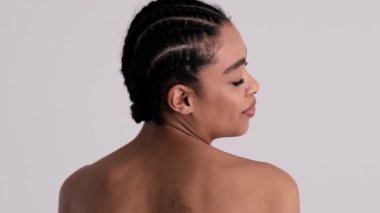 Gülümseyen, yarı çıplak bir kadının arka plan görüntüsü stüdyodaki gri arka planda tek başına kameraya dönüyor.