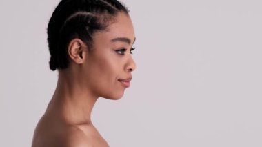 Pozitif, yarı çıplak bir kadının yan görüntüsü stüdyodaki gri arka planda tek başına kameraya dönüyor.