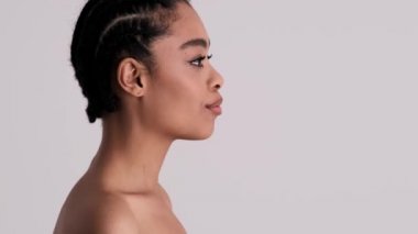 Hoş, genç, yarı çıplak bir kadının yan görüntüsü stüdyodaki gri arka planda tek başına duran bir hava öpücüğü gönderiyor.