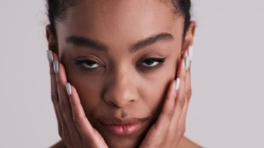 Mutlu, yarı çıplak bir kadının yakın plan görüntüsü stüdyodaki gri arka planda tek başına duran kameraya bakıyor.