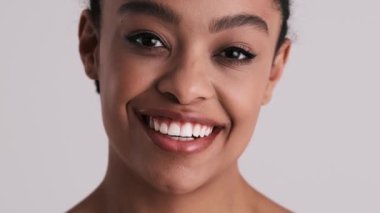 Güzel, yarı çıplak bir kadının yakın plan görüntüsü stüdyodaki gri arka planda tek başına kameraya poz veriyor.