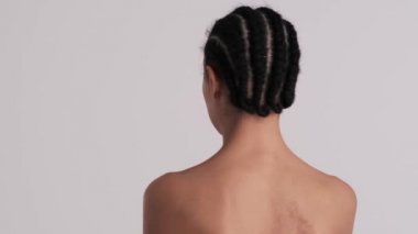 Gülümseyen yarı çıplak bir kadının arka plan görüntüsü stüdyodaki gri bir arka planda izole bir şekilde kameraya döndüğü sırada 