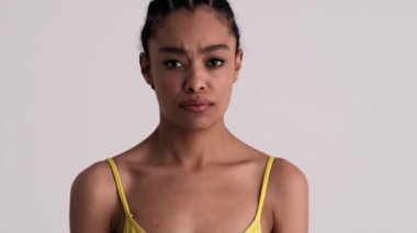 Alıngan bir kadın kafasını sallıyor. Stüdyonun gri arka planında tek başına duruyor.